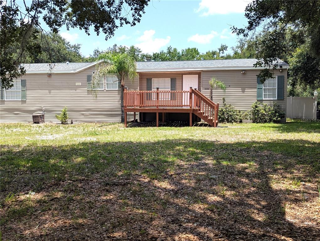 A single-story manufactured home with tan siding, green shutters, and a wooden front deck — 30517 CLEARVIEW DRIVE, WESLEY CHAPEL, FL