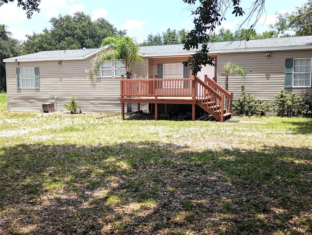 A tan manufactured home features a wooden deck with stairs leading to the front entrance — 30517 CLEARVIEW DRIVE, WESLEY CHAPEL, FL