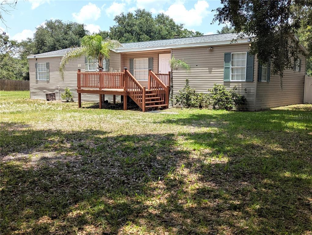 A single-story manufactured home with tan siding and a wooden deck entrance — 30517 CLEARVIEW DRIVE, WESLEY CHAPEL, FL