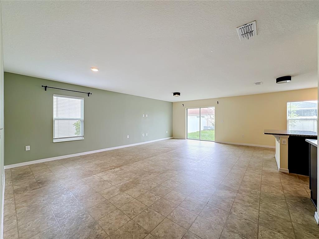 A living room features light green walls, tile flooring, a wall-mounted television, and sliding doors — 10624 MASSIMO DRIVE, WIMAUMA, FL