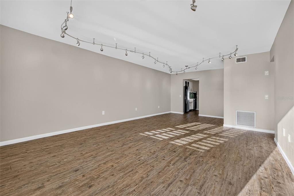 This virtually staged living room features light wood floors, a sectional sofa, and track lighting — 6015 19TH STREET N UNIT 215, ST PETERSBURG, FL
