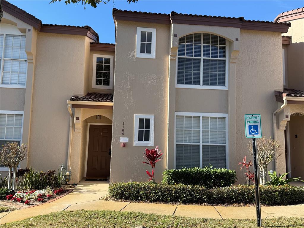 A two-story tan stucco townhouse features a brown front door and a reserved parking sign — 3164 TAMARIND CIRCLE, KISSIMMEE, FL