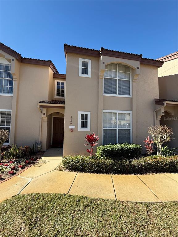 A two-story tan stucco townhouse features a front entrance and a small landscaped yard — 3164 TAMARIND CIRCLE, KISSIMMEE, FL