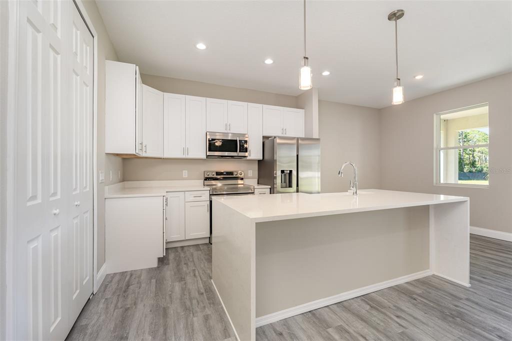 A modern kitchen features white cabinetry, stainless steel appliances, a quartz island, and gray flooring — 900 LAVA STREET SE, PALM BAY, FL