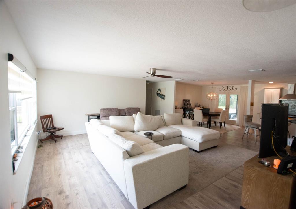 A living room with light wood-look flooring, a large white sectional sofa, and dining area — 308 WENDI LANE, RUSKIN, FL