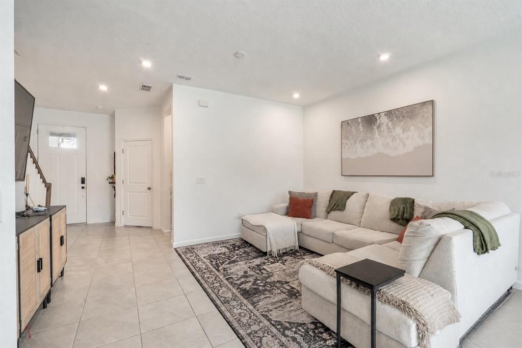 A living room features a white sectional sofa, a patterned area rug, and tile flooring — 1157 SEASIDE MIST TRAIL, KISSIMMEE, FL