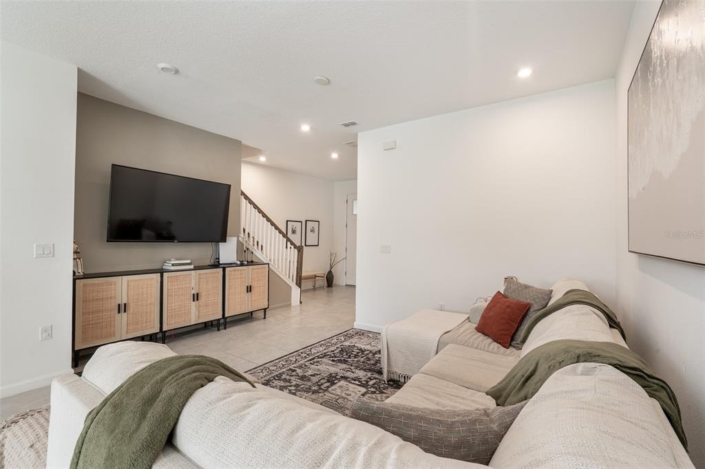 A living room features a beige sectional sofa, a television on a cabinet, and stairs — 1157 SEASIDE MIST TRAIL, KISSIMMEE, FL