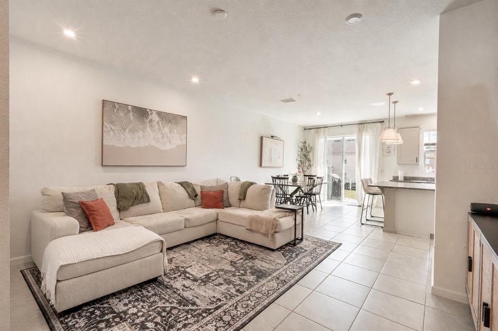 A living room with a sectional sofa, area rug, and an adjacent dining and kitchen area — 1157 SEASIDE MIST TRAIL, KISSIMMEE, FL