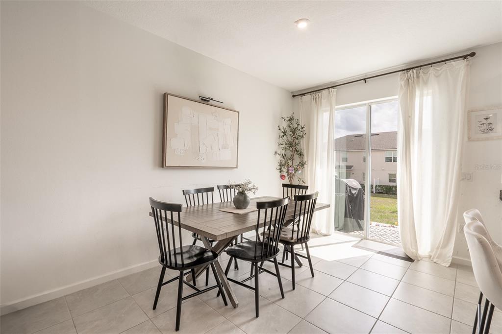 A dining room features a wooden table, black spindle chairs, tile flooring, and sliding glass doors — 1157 SEASIDE MIST TRAIL, KISSIMMEE, FL