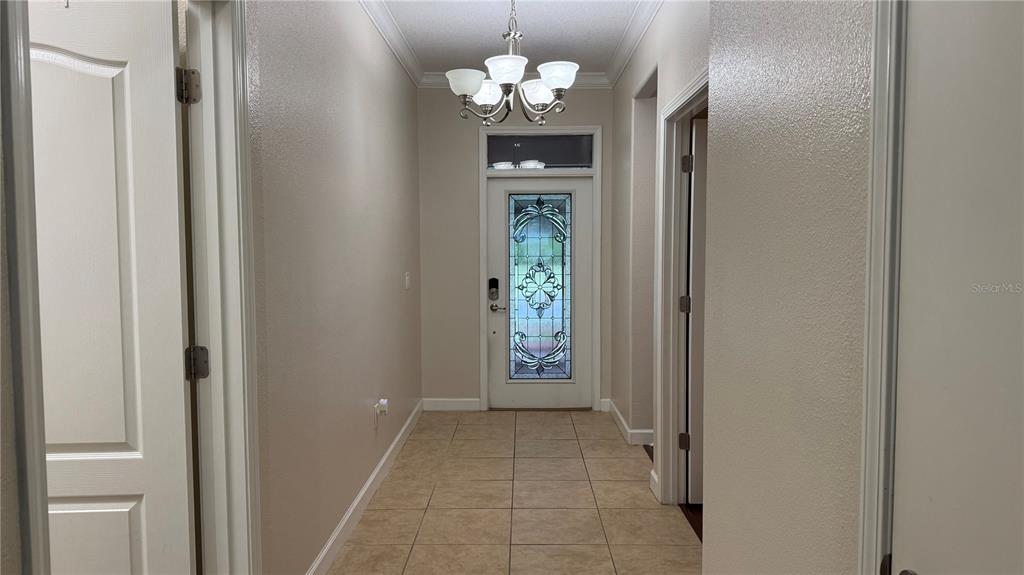A tiled entryway features a chandelier, a wooden display cabinet, and a glass-paneled front door — 4056 SERENA LANE, CLERMONT, FL