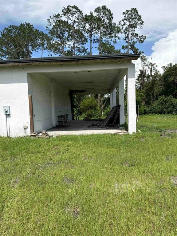 An open-sided concrete carport stands on a grassy lot with trees in the background — 1116 N HIGHWAY 17 UNIT 1, PALATKA, FL