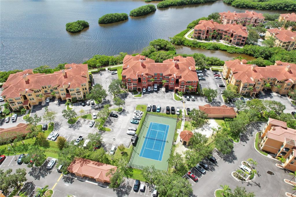 An aerial view shows multi-story residential buildings, a tennis court, and parking lots near water — 2724 VIA MURANO UNIT 622, CLEARWATER, FL