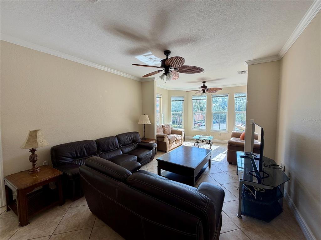 A living room features dark leather furniture, tile flooring, two ceiling fans, and large windows — 2724 VIA MURANO UNIT 622, CLEARWATER, FL