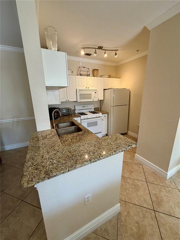 A kitchen features granite countertops, white cabinetry, a white stove, and a refrigerator — 2724 VIA MURANO UNIT 622, CLEARWATER, FL