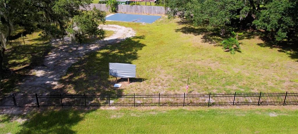 An aerial view shows a vacant, grassy lot enclosed by a black metal fence — 1550 S TANNER ROAD, ORLANDO, FL