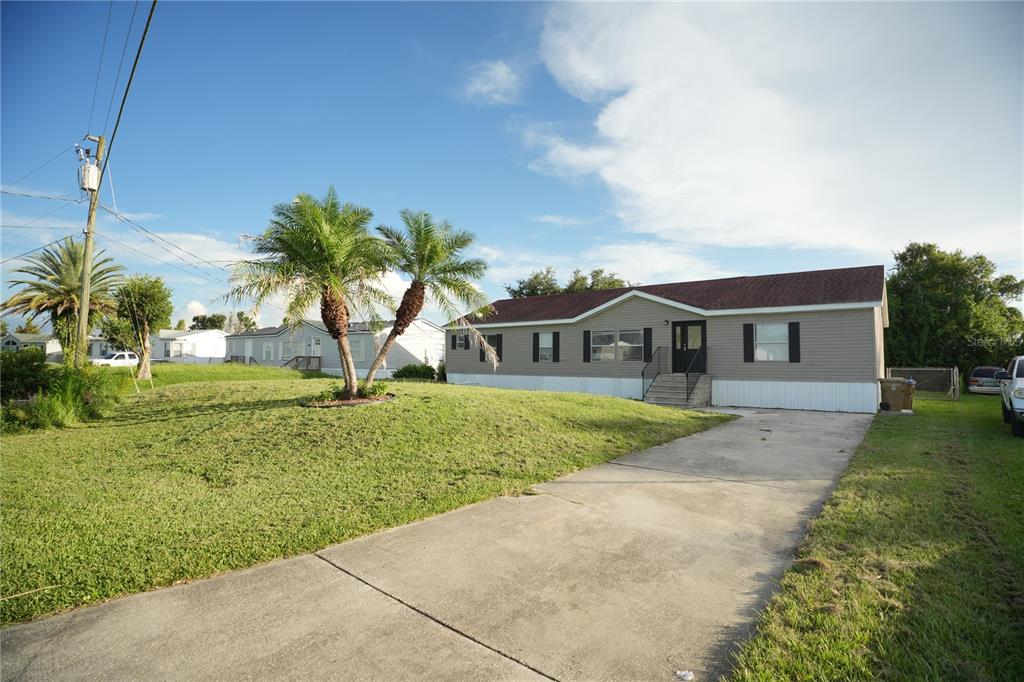 A single-story manufactured home with light gray siding and a concrete driveway sits on a lawn — 1124 DARA CAY DRIVE, KISSIMMEE, FL