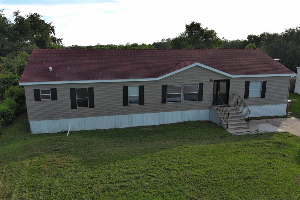 An exterior view of a single-story manufactured home with tan siding and a red roof — 1124 DARA CAY DRIVE, KISSIMMEE, FL