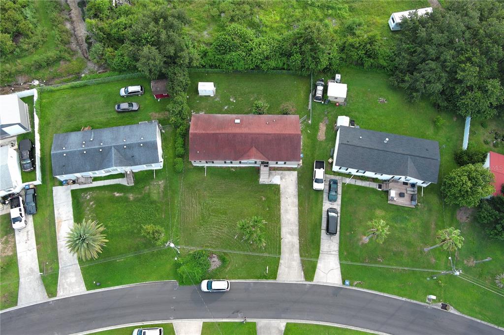 An aerial view shows three houses with driveways and lawns along a curved residential street — 1124 DARA CAY DRIVE, KISSIMMEE, FL
