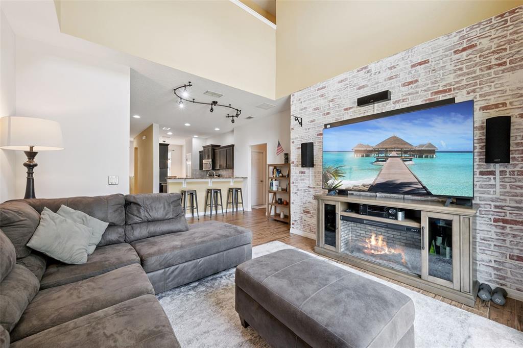 A living room features a brick accent wall, a large television, and a sectional sofa — 4880 POOLSIDE DRIVE, ST CLOUD, FL