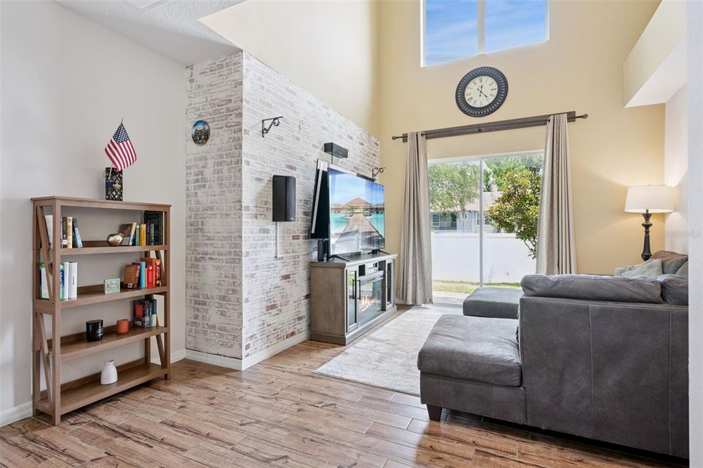 A living room features a whitewashed brick accent wall, wood-look tile flooring, and vaulted ceilings — 4880 POOLSIDE DRIVE, ST CLOUD, FL