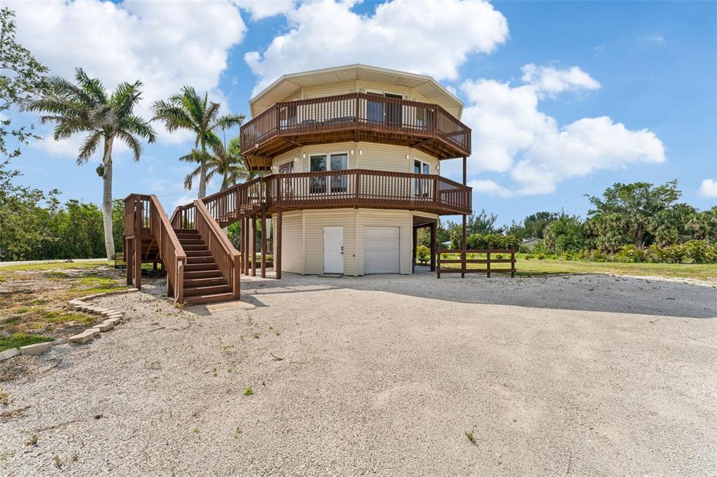 An elevated, octagonal house with two wrap-around wooden decks, stairs, and a gravel driveway — 16361 STRINGFELLOW ROAD, BOKEELIA, FL