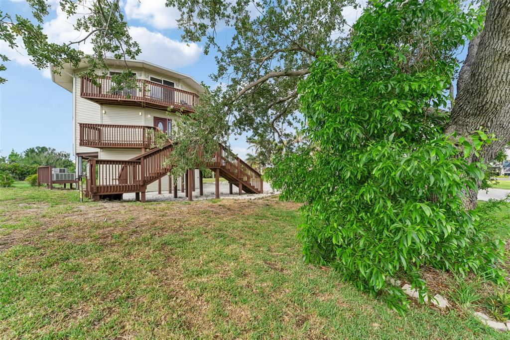 An elevated house with wooden decks and stairs stands in a grassy yard with trees — 16361 STRINGFELLOW ROAD, BOKEELIA, FL