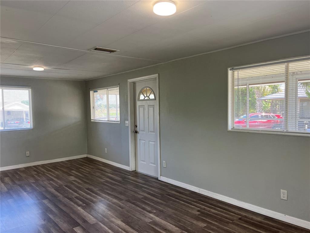 An empty room with gray walls, wood-look flooring, a white door, and multiple windows — 3731 STATE ROAD 60 E UNIT 23, LAKE WALES, FL