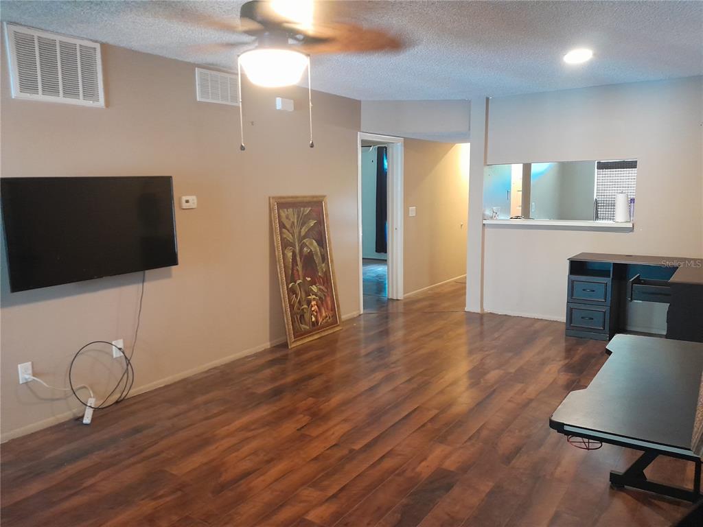 A living room with wood-look flooring, a ceiling fan, a wall-mounted television, and a desk — 25210 NORTHLAKE DRIVE UNIT 210, SANFORD, FL