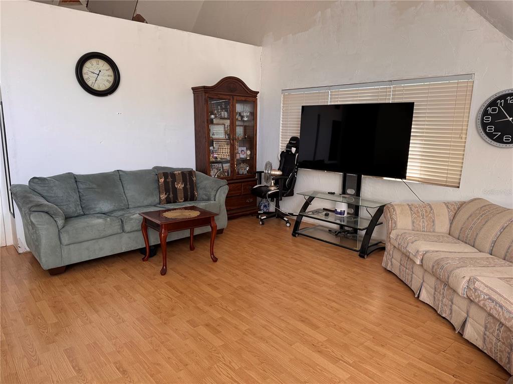 A living room features two sofas, a glass TV stand, a wooden cabinet, and wood flooring — 7923 18TH AVENUE E, PALMETTO, FL