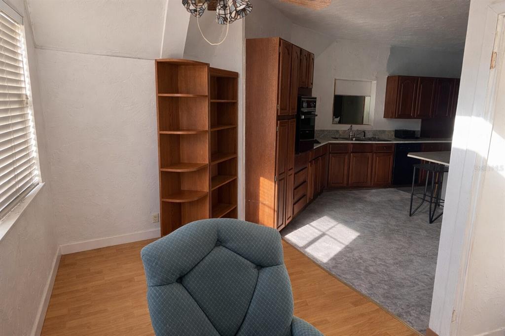 A blue armchair sits in a room with wood flooring next to a kitchen area — 7923 18TH AVENUE E, PALMETTO, FL