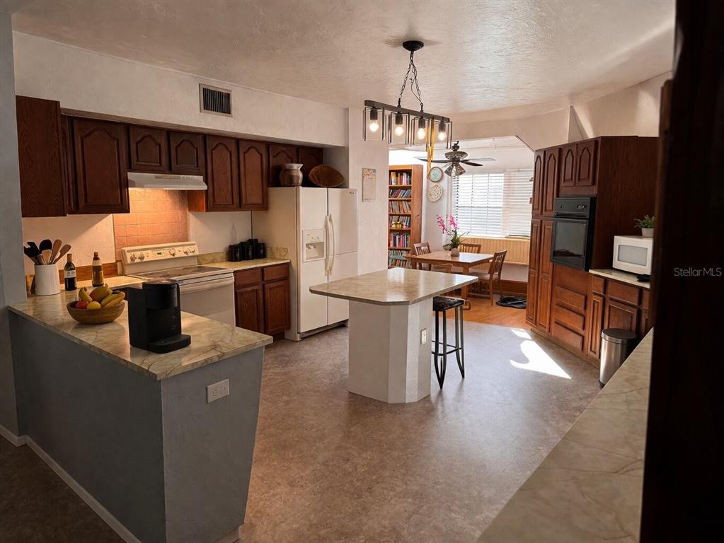 A kitchen with wood cabinets, a central island, and an adjacent dining area with windows — 7923 18TH AVENUE E, PALMETTO, FL