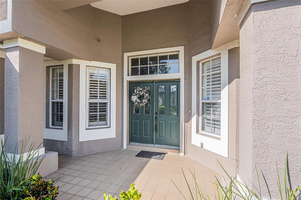 A covered entryway features a double green front door, tiled flooring, and white-trimmed windows — 7004 PINE HOLLOW DRIVE, MOUNT DORA, FL