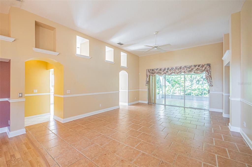 A spacious living room features high ceilings, tile flooring, and a large sliding glass door — 7004 PINE HOLLOW DRIVE, MOUNT DORA, FL