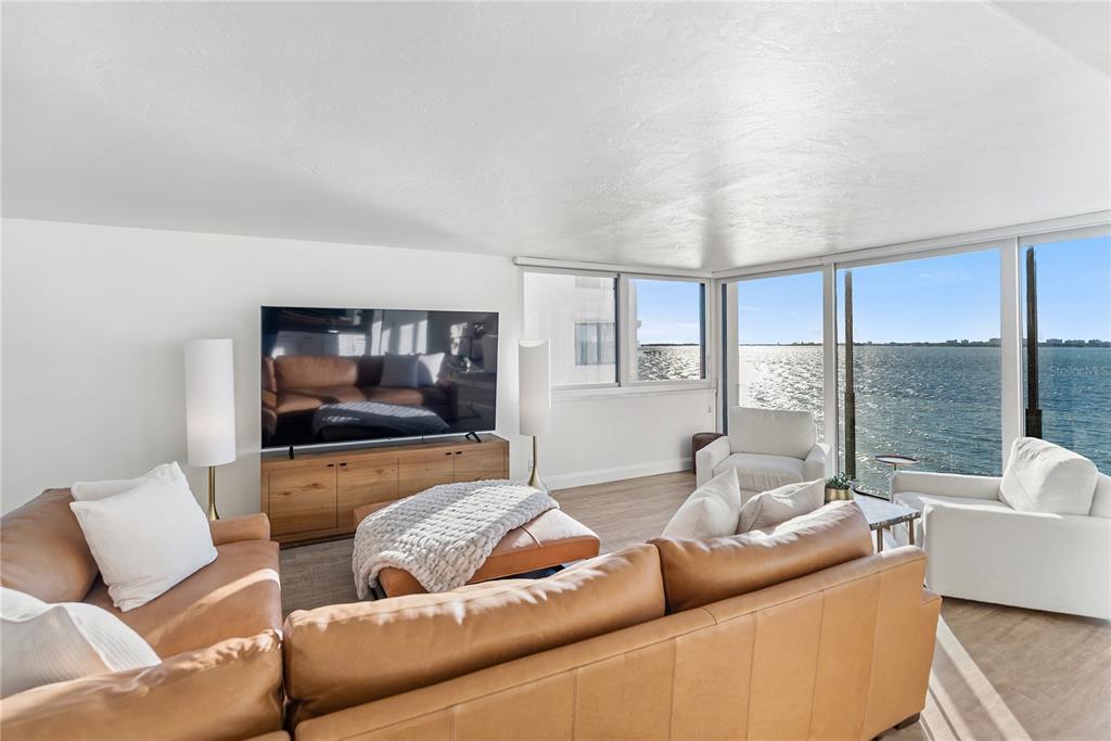A living room features a leather sectional, a television, and floor-to-ceiling windows overlooking the water — 101 SUNSET DRIVE UNIT 402, SARASOTA, FL
