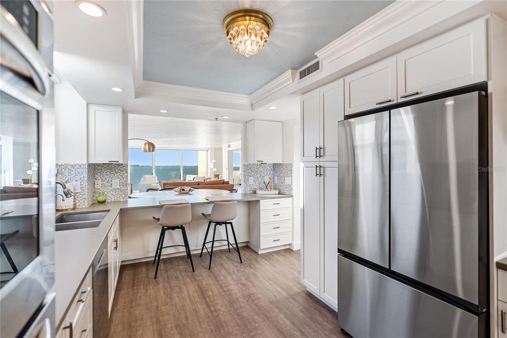 A modern kitchen features white cabinets, stainless steel appliances, a breakfast bar, and ocean views — 101 SUNSET DRIVE UNIT 402, SARASOTA, FL