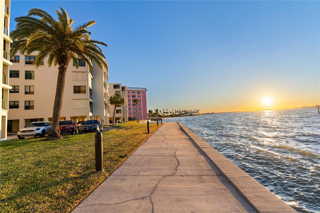 A concrete walkway runs along the water next to apartment buildings and a palm tree — 101 SUNSET DRIVE UNIT 402, SARASOTA, FL