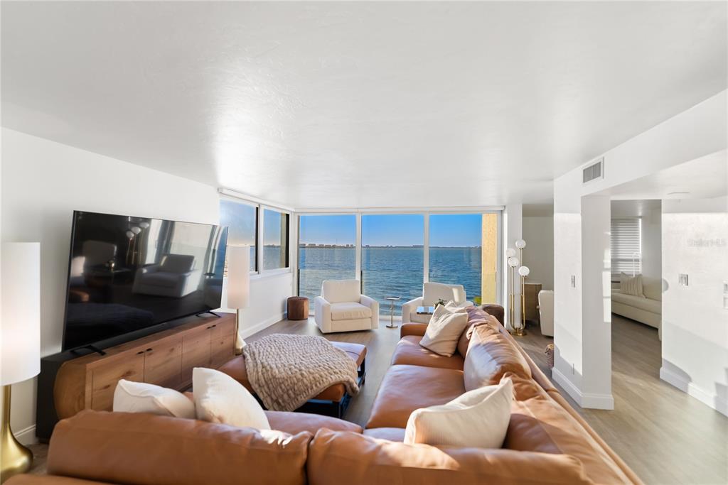 A living room features a leather sectional, a large television, and floor-to-ceiling windows overlooking water — 101 SUNSET DRIVE UNIT 402, SARASOTA, FL