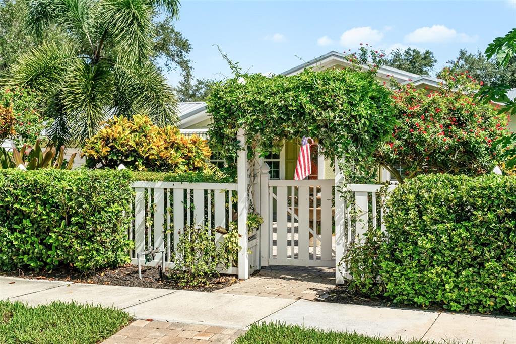 A white picket fence and gate are surrounded by lush green hedges and flowering plants — 1907 MAGNOLIA STREET, SARASOTA, FL