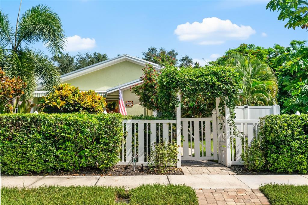 A light green house is partially obscured by a white picket fence and lush landscaping — 1907 MAGNOLIA STREET, SARASOTA, FL