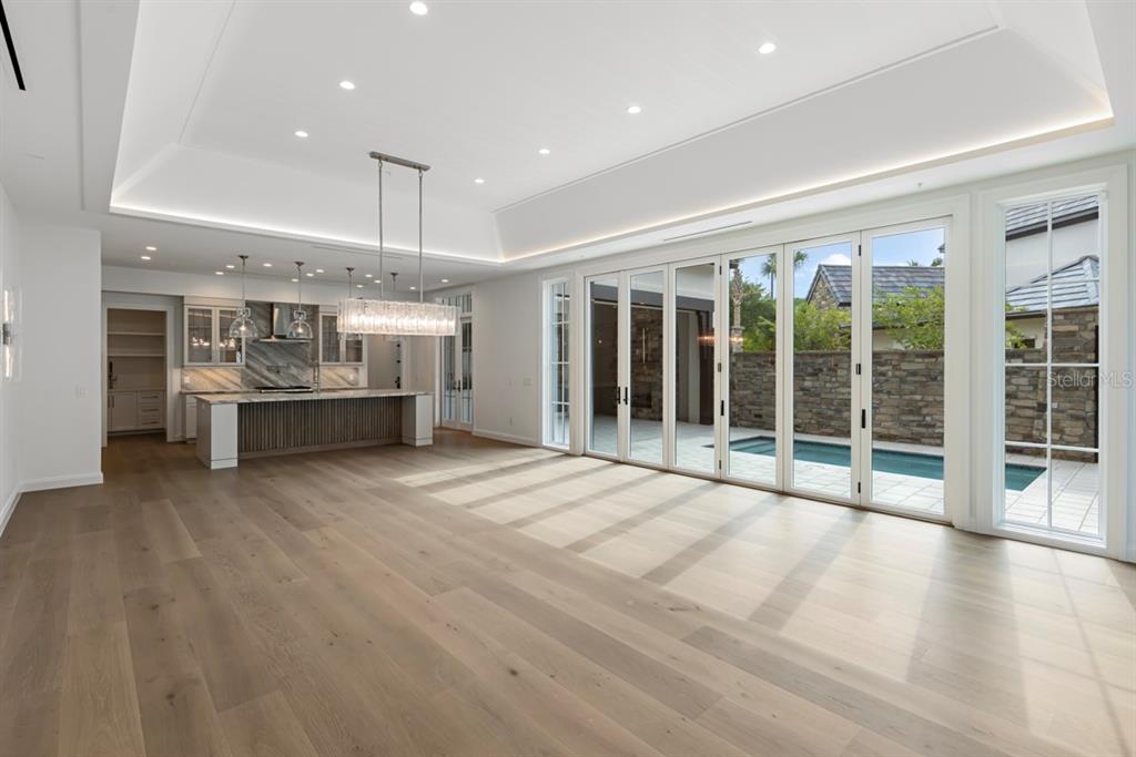 A spacious, modern open-concept living area with light wood floors, a tray ceiling, and kitchen — 10335 WINTER SPARKLE CIRCLE, GOLDEN OAK, FL