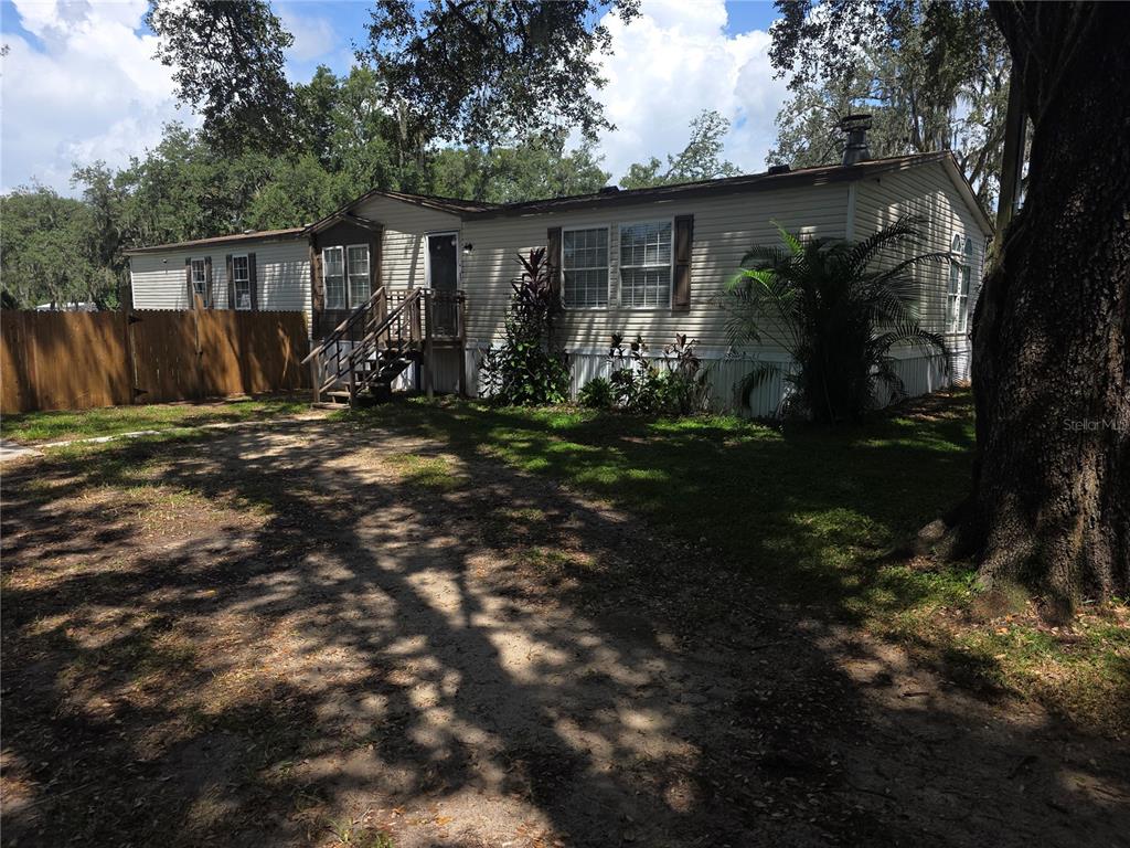 A single-story manufactured home with light siding, a wooden deck, and a fenced yard — 1020 BRINWOOD DRIVE, SEFFNER, FL