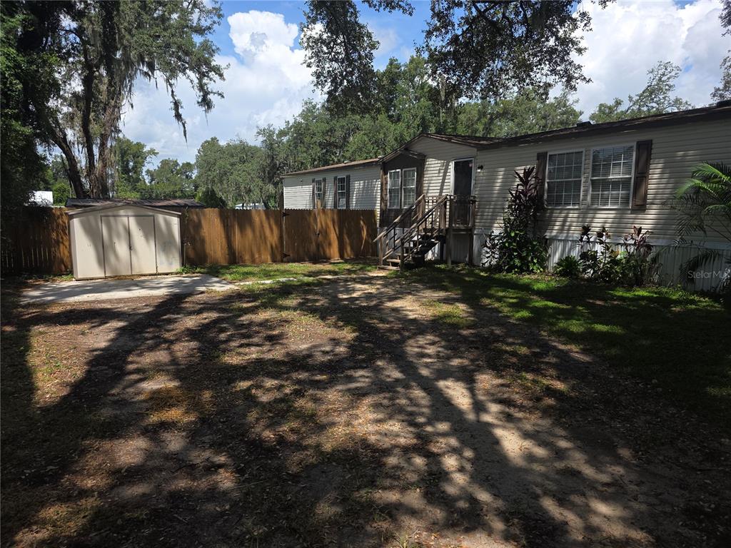A mobile home exterior with a wooden fence, a storage shed, and a concrete pad — 1020 BRINWOOD DRIVE, SEFFNER, FL