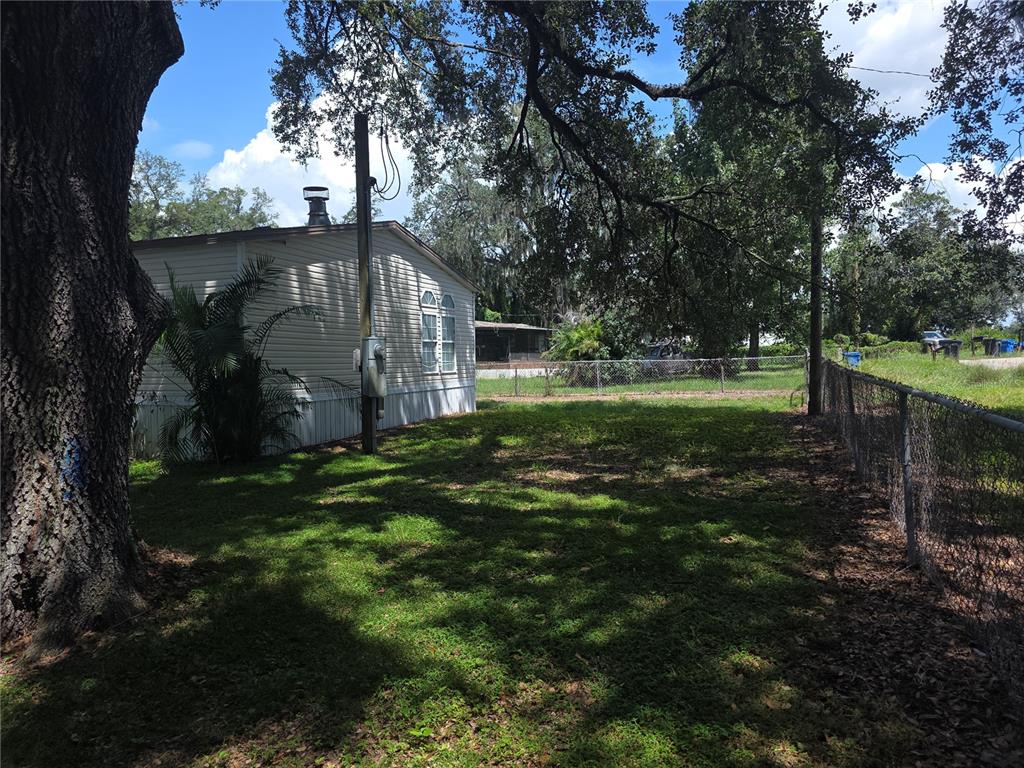 A side view of a mobile home with a large tree and a chain-link fence — 1020 BRINWOOD DRIVE, SEFFNER, FL
