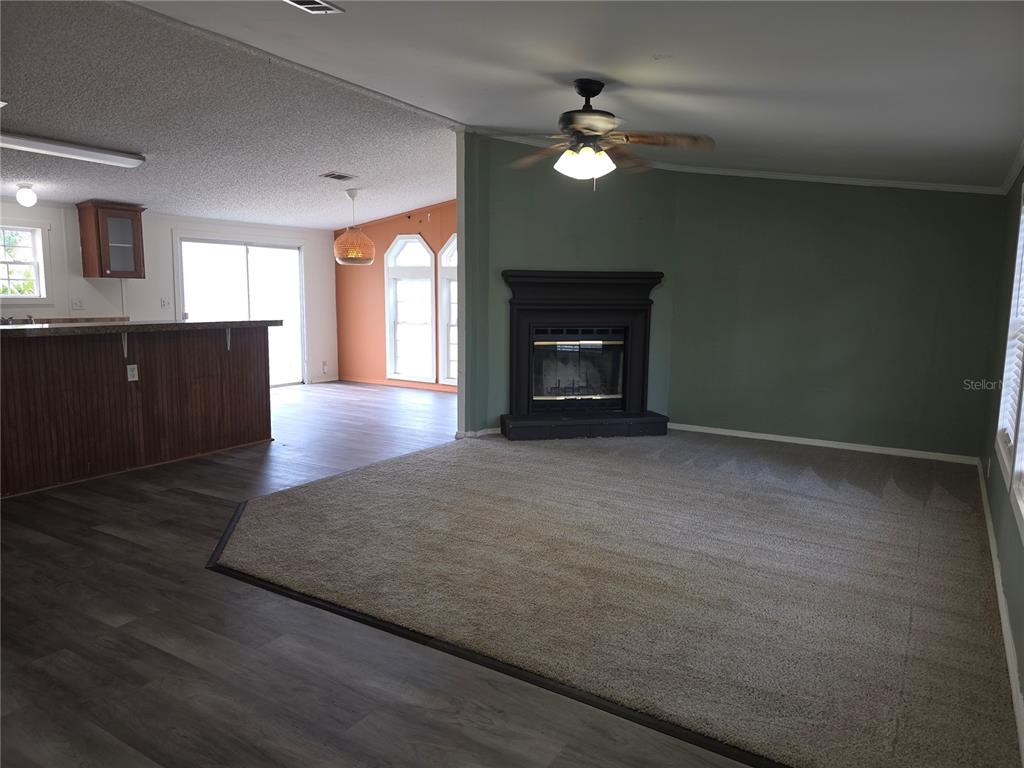 A living room with a fireplace and carpeted floor transitions into a kitchen with wood flooring — 1020 BRINWOOD DRIVE, SEFFNER, FL