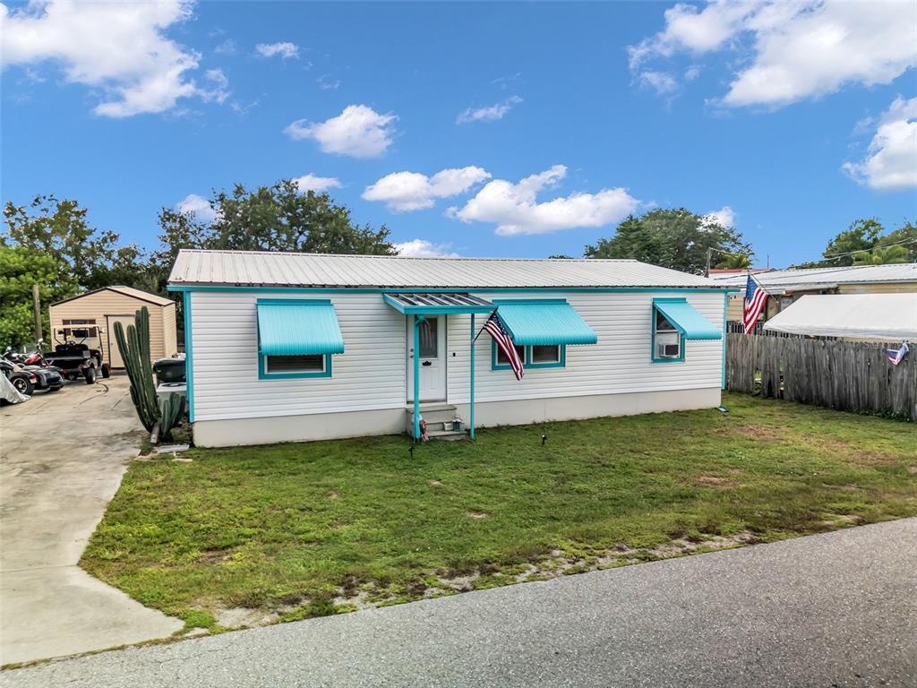A single-story mobile home with white siding, turquoise accents, and metal awnings under a blue sky — 1212 9TH STREET, OKEECHOBEE, FL