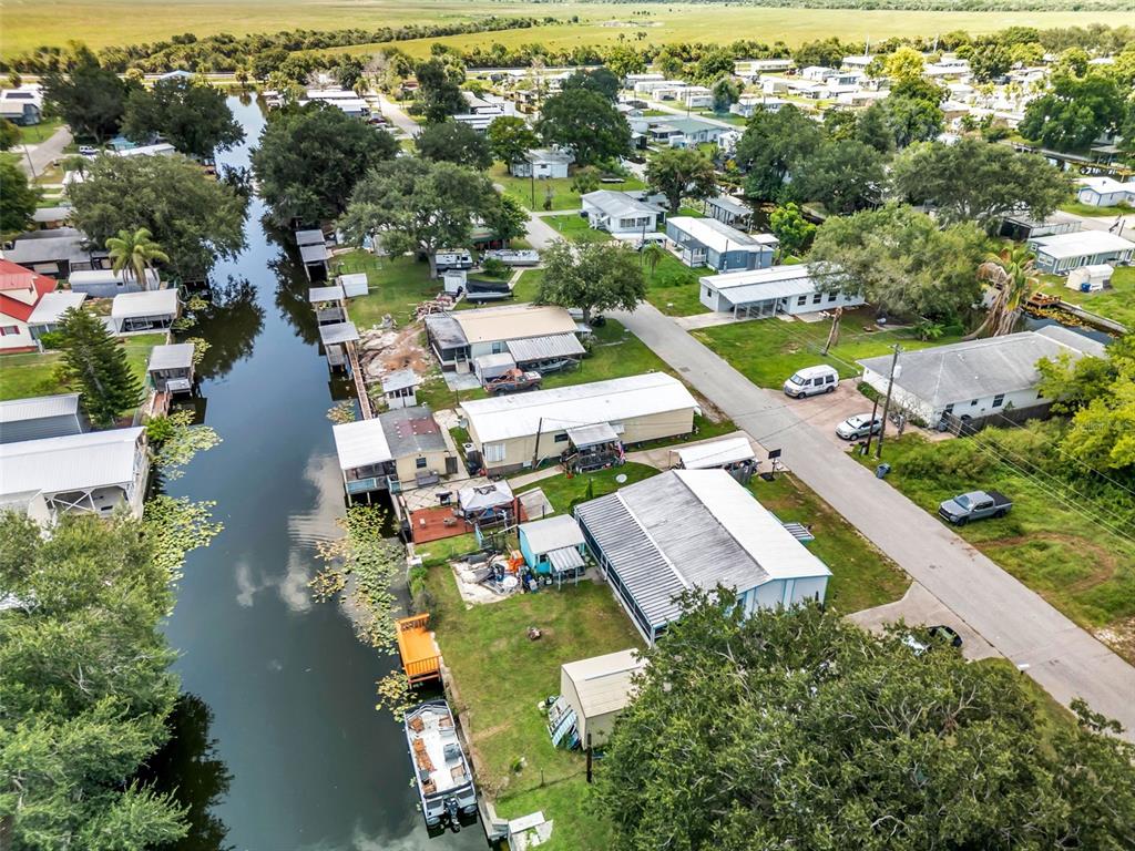 An aerial view shows a canal-side neighborhood with mobile homes, boat docks, and parked vehicles — 1212 9TH STREET, OKEECHOBEE, FL