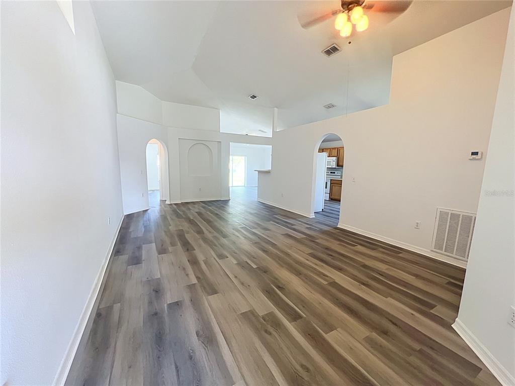 An empty living room with vaulted ceilings, white walls, and wood-look vinyl plank flooring — 5641 ROYAL HILLS DRIVE, WINTER HAVEN, FL