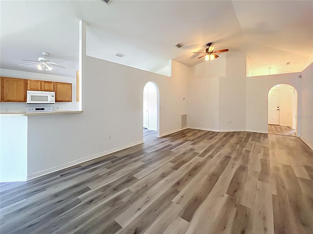 An open-concept living area features vaulted ceilings, wood-look flooring, and an adjacent kitchen with cabinets — 5641 ROYAL HILLS DRIVE, WINTER HAVEN, FL