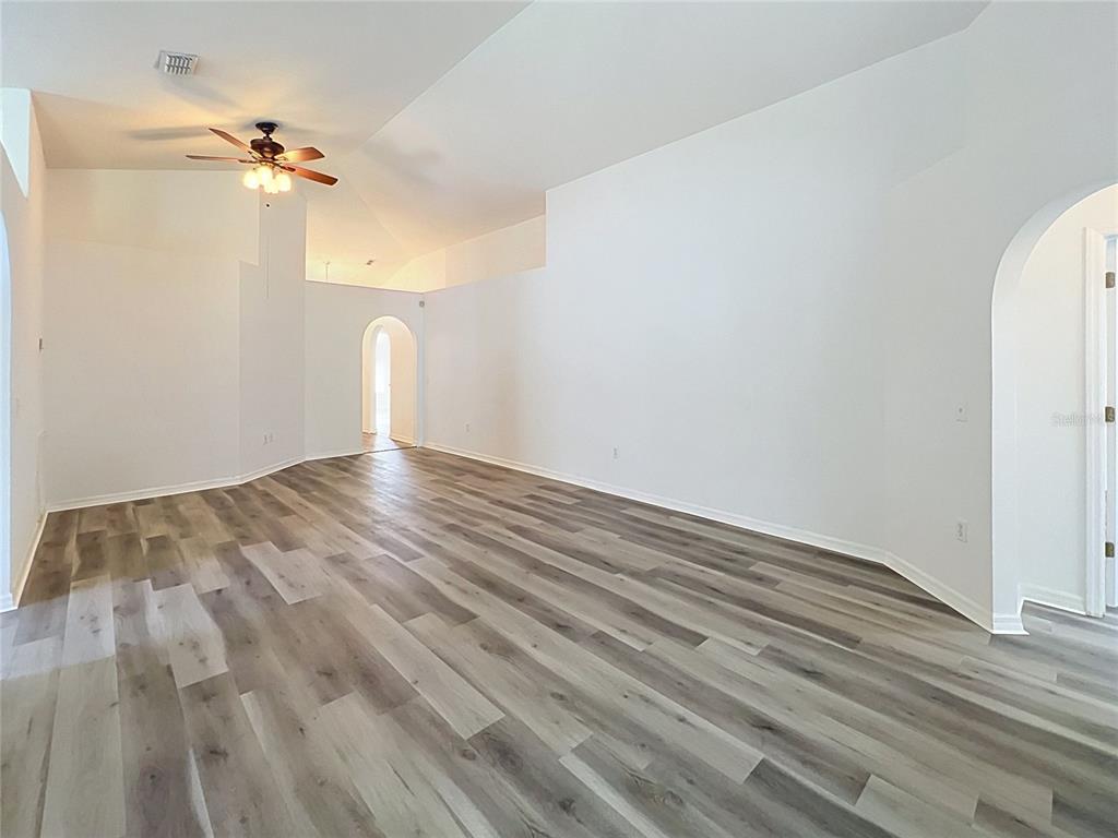 An empty room with vaulted ceilings, light wood-look flooring, and an arched doorway — 5641 ROYAL HILLS DRIVE, WINTER HAVEN, FL