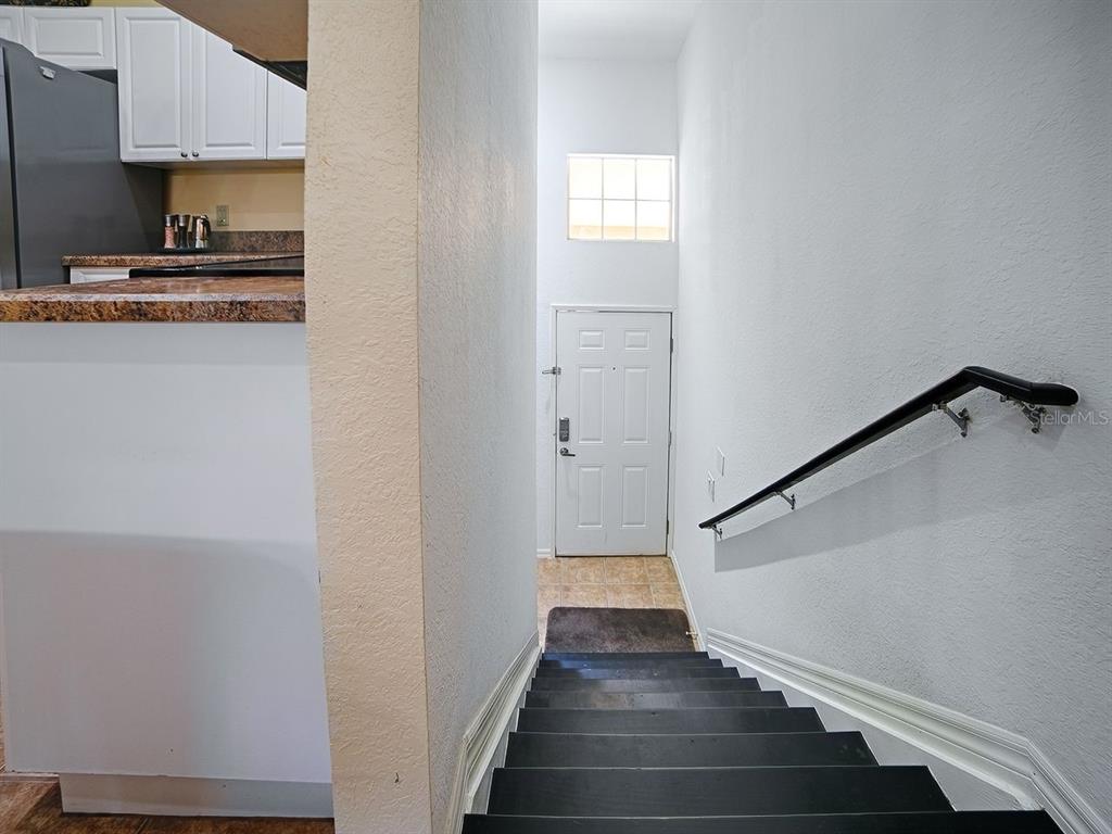 A staircase with dark treads leads down to a white front door and entryway — 5408 ADMIRAL WAY UNIT 11-202, OXFORD, FL